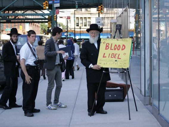 A photo of a man holding a "Blood Libel" sign during a heated circumcision hearing in 2013