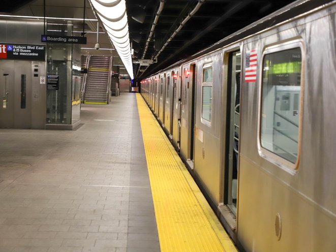 An empty subway station, with no one on the platform, with an E train waiting