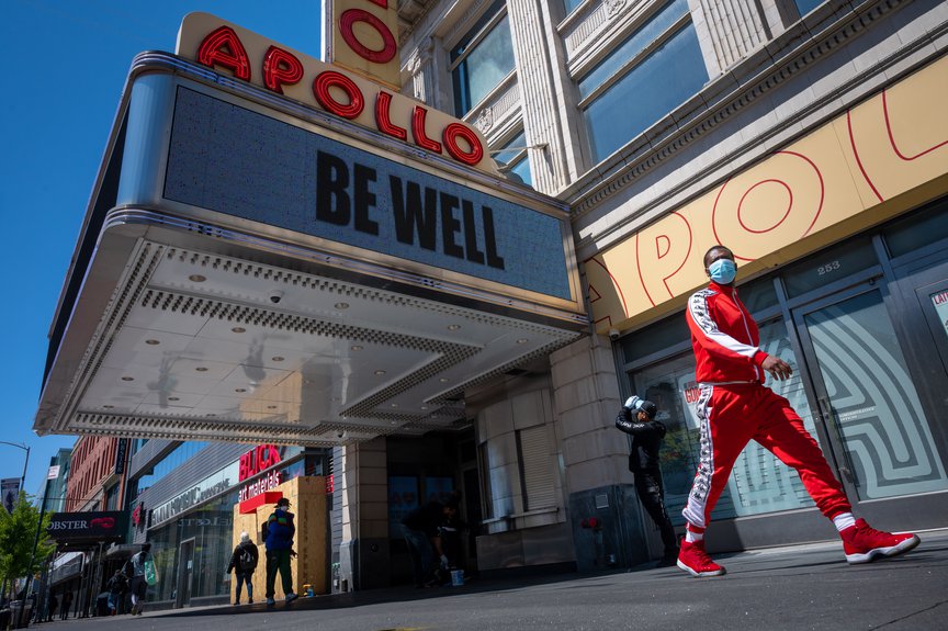 A man wearing a mask walks by the Apollo Theatre's marquee, which says "BE WELL"