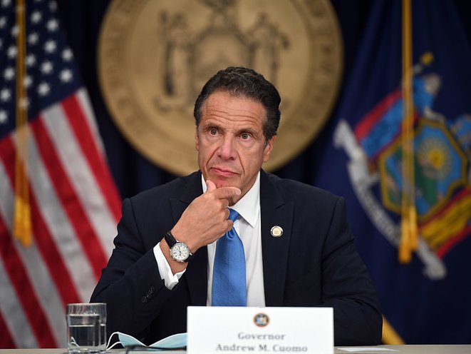Governor Andrew Cuomo at a table speaking with flags and the NY state seal behind him