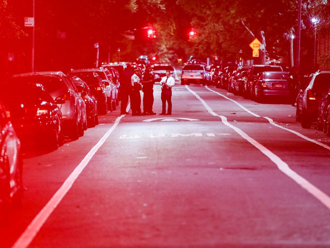 Police officers bathed in lights from flashing emergency lights respond to a crime scene were two individuals were injured by gunfire in Brooklyn on July 18th, 2020.