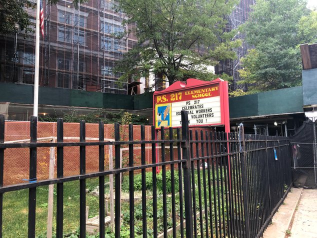 Outside PS 217, a red brick building with scaffolding over it, a sign salutes teachers
