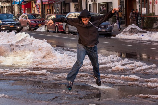 A man wearing shoes elegantly jumps over a slushy lagoon in NYC.