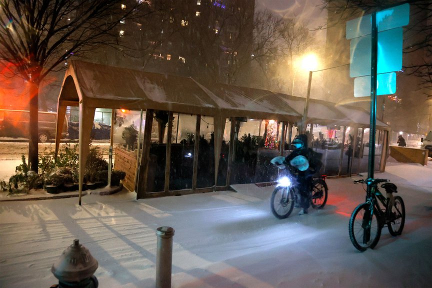 A delivery cyclist rides through the snow next to a shuttered outdoor dining setup in the East Village during last month's snowstorm.