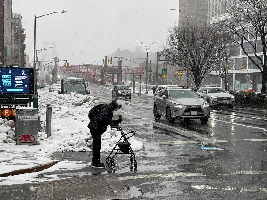 A person using a walker attempts to cross a slushy corner of Delancey Street in Manhattan.