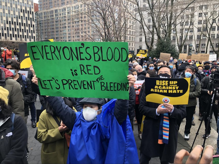 Andrew Yang wears a mask and holds a sign denouncing anti-Asian violence next to a person holding a sign that says "Everyone's Blood is red"