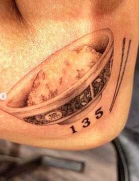 A tattoo of a rice bowl, chops, and the numerals 135 on an arm