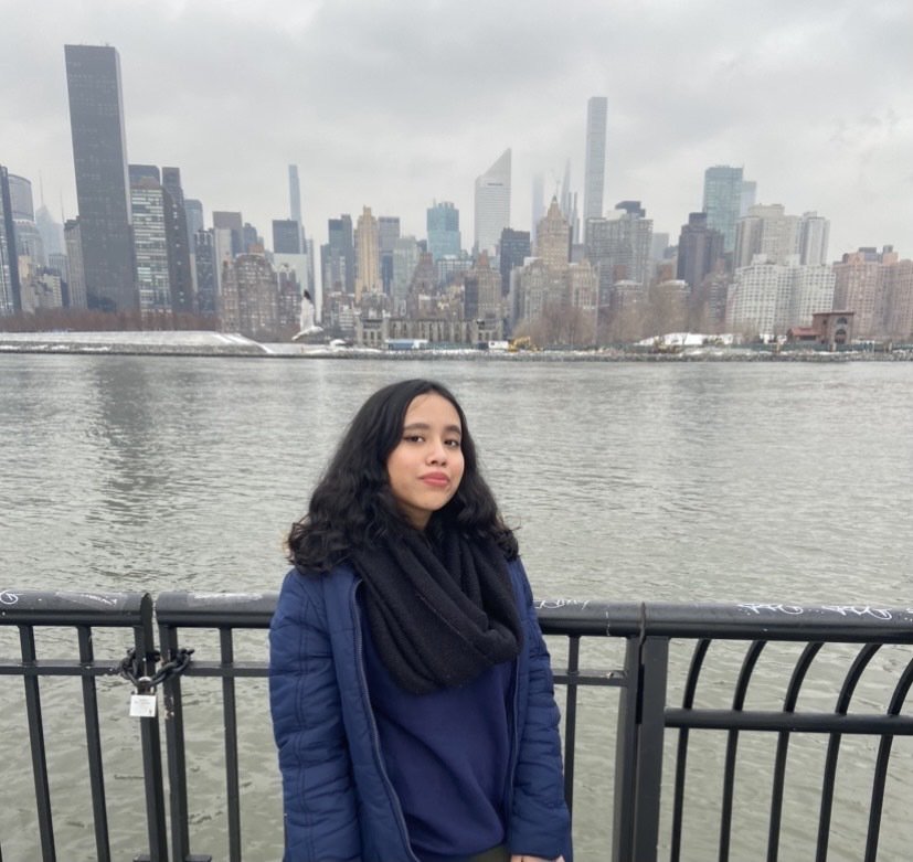 Siara Chowdhury stands in front of the East River, with the Manhattan skyline behind her