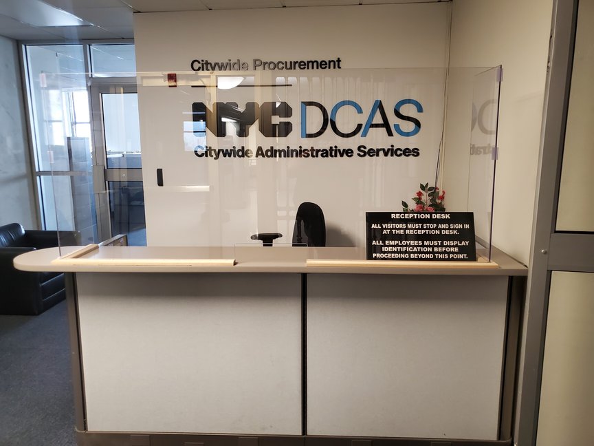 A cubicle with the Department of Citywide Administrative Services sign behind it on a wall, with a Plexiglas barrier