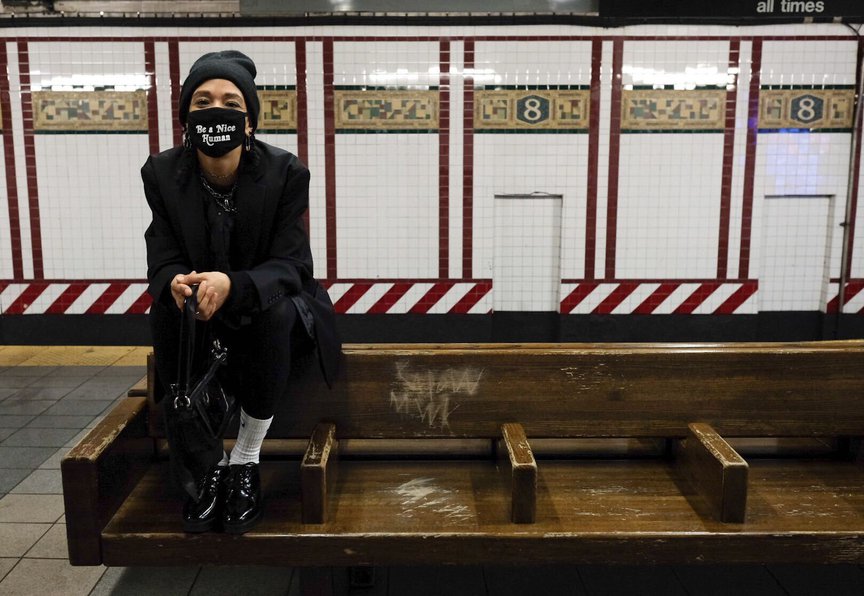 Vanessa Redmond, sitting on the back of a subway bench while in a mask and wearing a beanie on her head