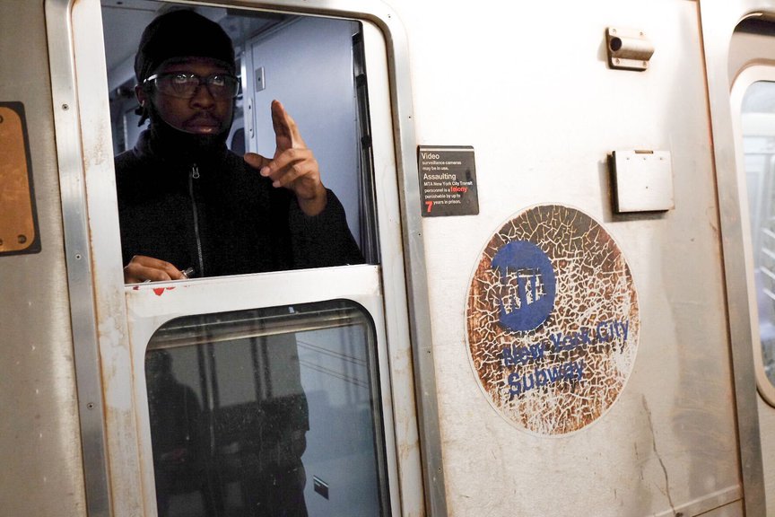 An MTA conductor gestures from his subway compartment