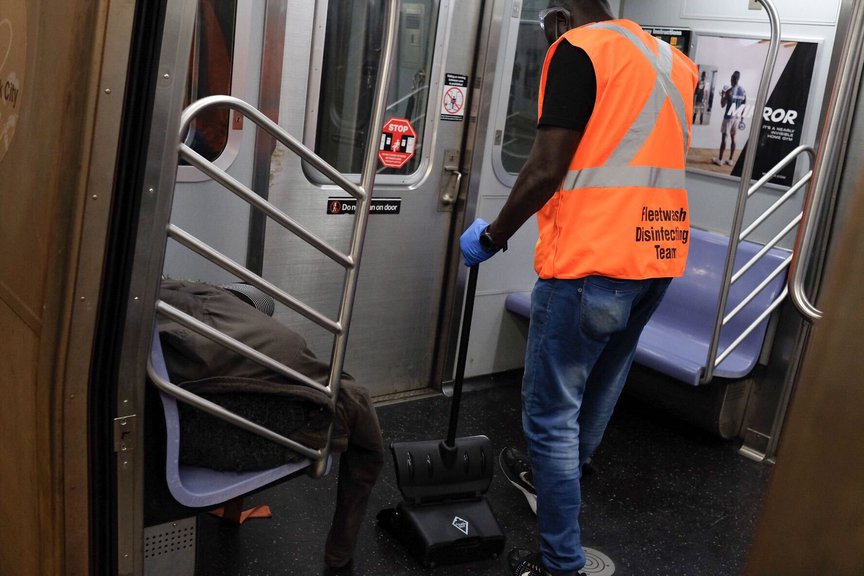 An MTA worker is seen standing next to a person sleeping on a subway bench