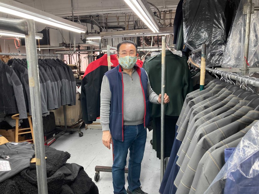 Michael Lee is seen, wearing a mask and standing next to rows of suits
