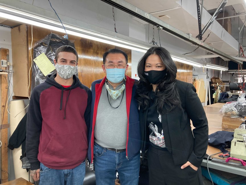 Mike Cardillo, Michael Lee, and Lisa Sun all wear masks and pose for a photograph inside the factory