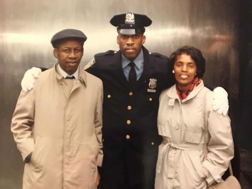 Rodney Harrison stands in his blue NYPD uniform with his arms around his parents, who are wearing tan coats