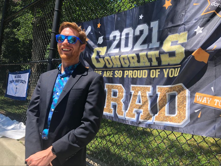 Kyle Brillante smiles while standing in front of a sign that says 2021 Congrats Grads