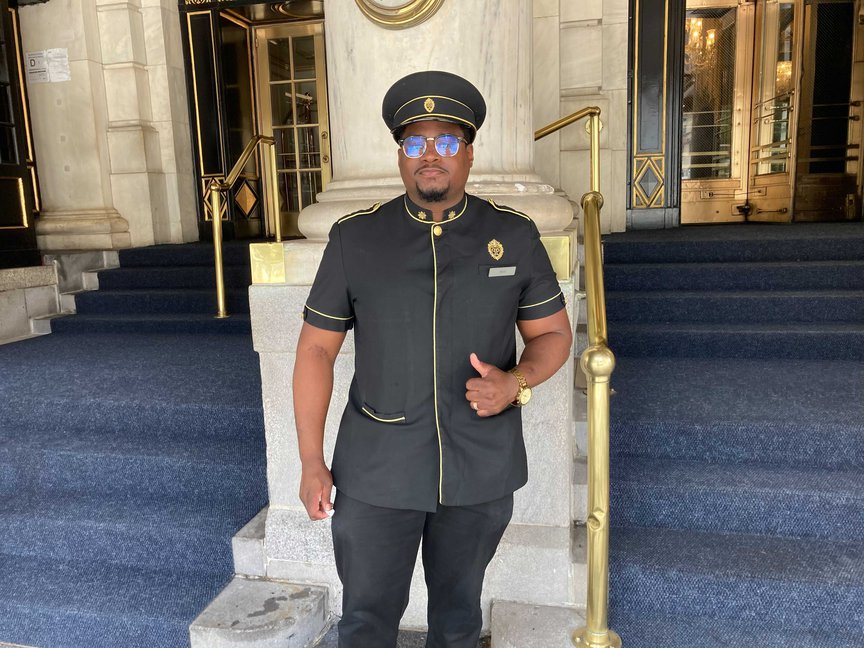 A Black male doorman in his Plaza uniform and hat outside the hotel