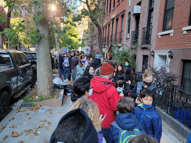 A line of students and parents or guardians on a sidewalk in Gramercy