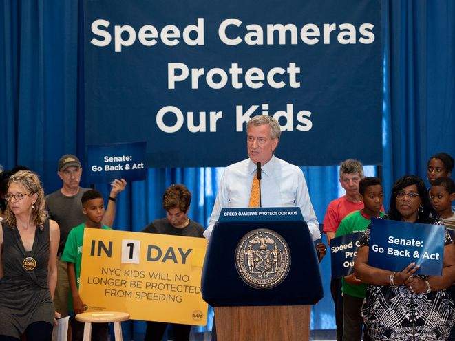 Mayor de Blasio with supporters in front of a sign that says "Speed Cameras save lives"